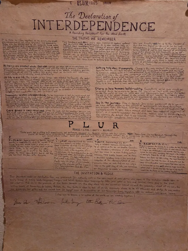 The original Declaration of Interdependence: a large sheet of parchment pinned to a wall, hand-lettered in ink, headed E Pluribus Unum, with sections titled The Truths We Remember, PLUR — Peace, Love, Unity, Respect — and The Invitation & Pledge, signed at the foot by hand.